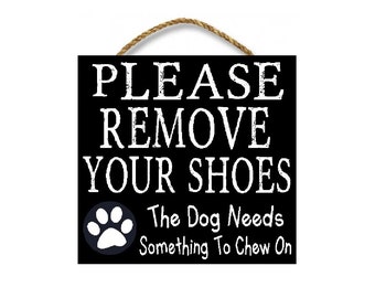 May include: Black and white sign with the text "PLEASE REMOVE YOUR SHOES The Dog Needs Something To Chew On". A white paw print is in the bottom left corner.
