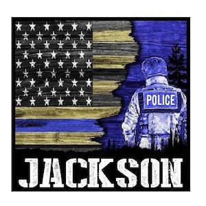 Puede incluir: Diseño gráfico con la bandera estadounidense, una franja azul y dorada, un oficial de policía y el nombre "JACKSON" en letras blancas. La bandera tiene una textura de madera desgastada.