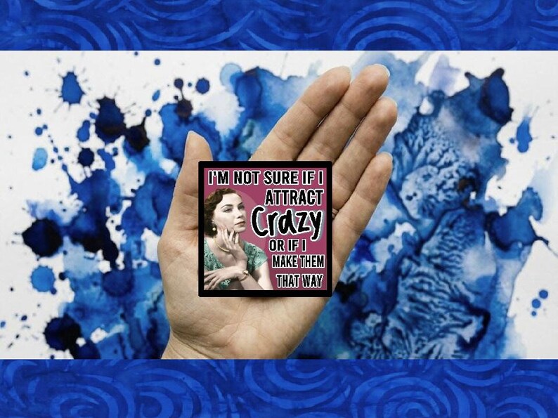 May include: A square black sticker with the text "I'M NOT SURE IF I ATTRACT Crazy OR IF I MAKE THEM THAT WAY" and a vintage image of a woman. The sticker is held in a hand against a blue and white watercolor background.