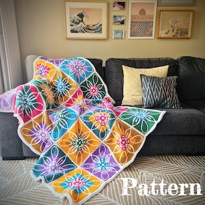 Puede incluir: Una manta de crochet colorida con un patrón floral en tonos de rosa, morado, amarillo, verde y azul. La manta está drapeada sobre un sofá con almohadas.