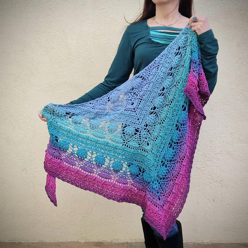 Pu&ograve; includere: Uno scialle all'uncinetto con un gradiente di rosa, blu e viola. Lo scialle &egrave; realizzato con un delicato motivo a pizzo e ha un bordo a frangia.