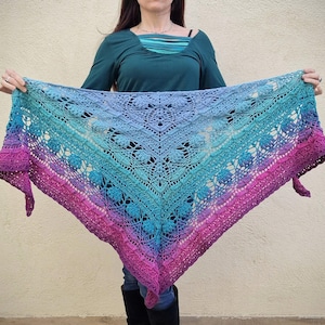 Pu&ograve; includere: Uno scialle triangolare all'uncinetto con un gradiente di rosa, blu e viola. Lo scialle presenta un delicato motivo a pizzo e un bordo a frangia.