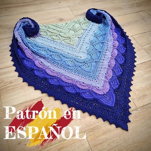 Puede incluir: Un chal de ganchillo azul, morado y verde con un borde festoneado. El chal está hecho con un hilo degradado y tiene un patrón delicado y de encaje. El texto "Patrón en ESPAÑOL" está escrito en la parte inferior de la imagen.
