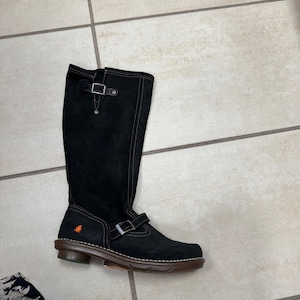 Puede incluir: Botas negras de ante hasta la rodilla con un detalle de hebilla y un pequeño logotipo naranja en el lateral.