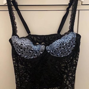 以下が含まれることがあります： 青い花柄の刺繍が施された黒いレースのランジェリートップ。トップは調節可能なストラップとバックルとアイの留め具が付いています。