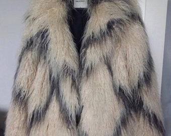 May include: A long-haired faux fur coat featuring a cream and dark gray chevron pattern. The coat has an open front design with a wide collar and a black interior lining. A white label at the neckline displays the text ONLY and the words life is forever.