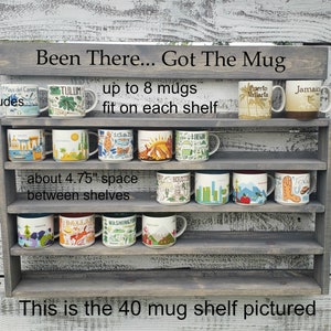 May include: A gray wooden shelf with four shelves, each holding up to eight mugs. The shelf is labeled "Been There... Got The Mug" and "This is the 40 mug shelf pictured". The shelves are filled with colorful mugs with city names and designs.