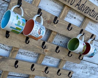 May include: Wooden mug rack with the text "Onward... To Adventure" painted on it. The rack has 15 hooks and is holding 4 mugs. The mugs are decorated with various designs and colors.