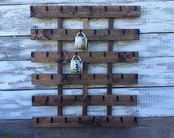 May include: A dark stained wooden mug rack with multiple rows of hooks. Two mugs hang from the rack. The rack is mounted on a white and blue painted wooden wall. The rack is designed to hold coffee mugs.