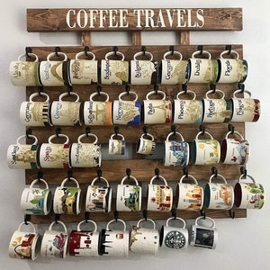 May include: A wooden wall-mounted coffee mug rack with the words "COFFEE TRAVELS" in white lettering. The rack holds 40 coffee mugs with various city and country designs.