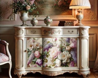 May include: A white painted wooden cabinet with ornate carvings and floral details. The cabinet has two drawers and two doors with a floral print. The cabinet is decorated with a floral arrangement in a silver vase and two small ceramic vases.