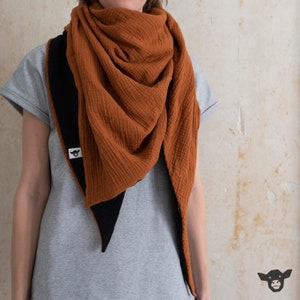 Könnte beinhalten: Ein rostfarbener Schal mit schwarzem Besatz. Der Schal ist aus einem weichen, strukturierten Stoff gefertigt und in Dreiecksform gefaltet.