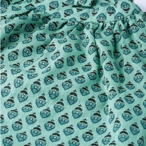 May include: Close-up of a teal blue fabric with a repeating pattern of small black flowers. The fabric has a slightly textured surface.