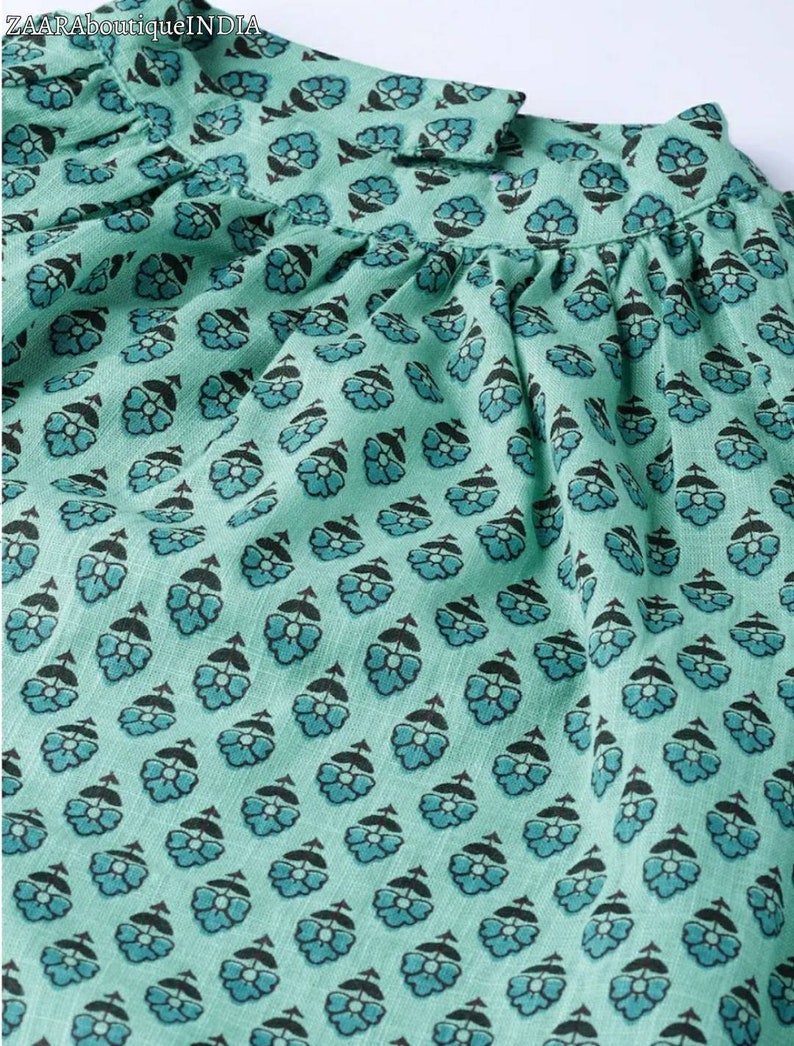 May include: Close-up of a teal blue fabric with a repeating pattern of small black flowers. The fabric has a slightly textured surface.