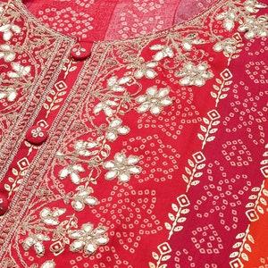 Puede incluir: Tela roja con un dise&ntilde;o bordado en oro con motivos florales y peque&ntilde;os adornos de espejo. La tela tiene un patr&oacute;n repetitivo de peque&ntilde;os puntos blancos.