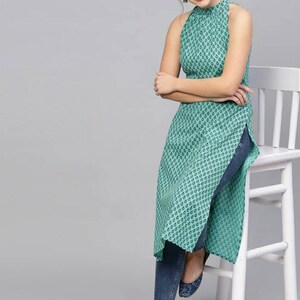 May include: A teal blue sleeveless top with a high neck and a geometric pattern. The top has a side slit and is worn with blue jeans.