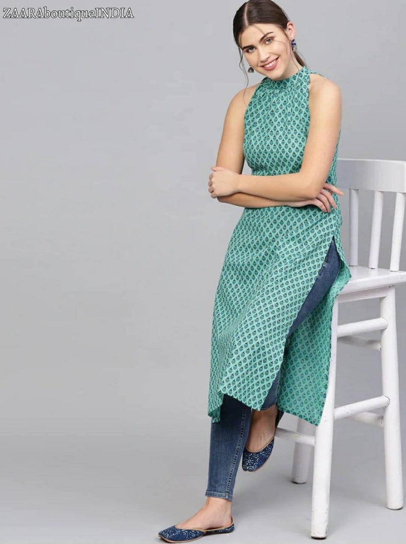 May include: A teal blue sleeveless top with a high neck and a geometric pattern. The top has a side slit and is worn with blue jeans.