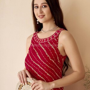 May include: A sleeveless, red dress with gold diagonal stripes and detailed embroidery around the neckline. The dress is accessorised with a round, woven handbag with a brown leather strap. The text "ZaraBoutiqueIndia" is visible.