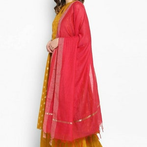 May include: A mustard yellow long dress with a floral pattern and a pink dupatta with gold trim. The dupatta has a fringe border.