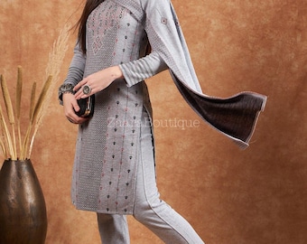 May include: A grey two-piece outfit. The long-sleeved tunic has detailed geometric patterns and matching trousers. The tunic features a detailed design on the chest and sleeves, with a flowing scarf. The outfit is paired with brown flats.