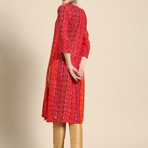 Puede incluir: Una blusa de manga larga roja y naranja con estampado floral y detalles dorados. La blusa tiene una abertura lateral y se combina con pantalones dorados.