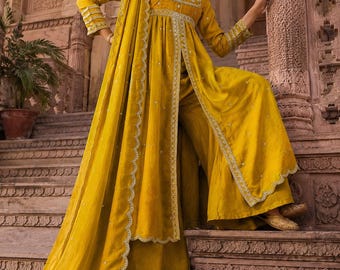 May include: A mustard yellow three-piece ensemble consisting of a long-sleeved tunic with a front slit, wide-leg trousers, and a matching dupatta. The outfit features intricate silver embroidery along the neckline, cuffs, and hemline borders.