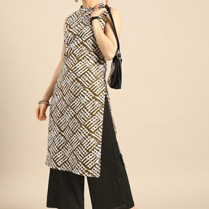 May include: A white and brown patterned sleeveless tunic top with a high neck and a side slit. The top is paired with black wide-leg pants and brown heeled sandals.
