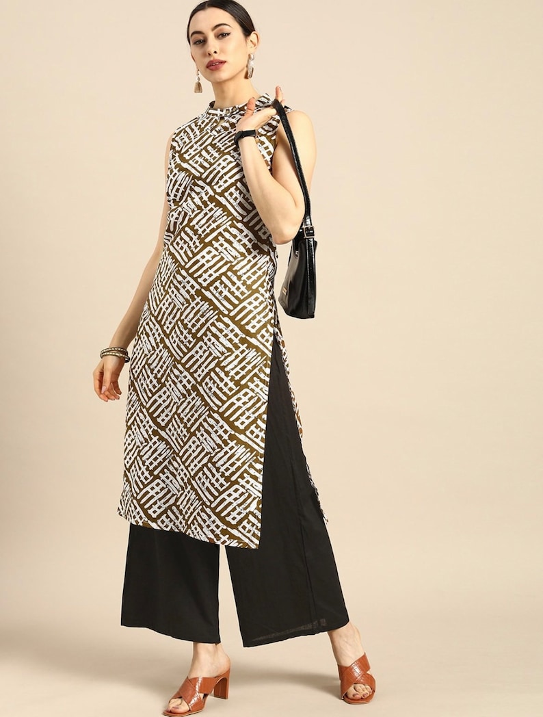 May include: A white and brown patterned sleeveless tunic top with a high neck and a side slit. The top is paired with black wide-leg pants and brown heeled sandals.