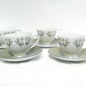 May include: Set of four white teacups and saucers with a green and gray floral pattern. The cups and saucers have a silver trim.