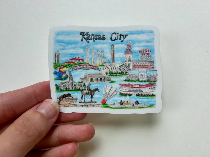 Puede incluir: Una ilustraci&oacute;n colorida de monumentos de Kansas City, incluyendo el Country Club Plaza, el Museo de Arte Nelson-Atkins, el Centro Kauffman para las Artes Esc&eacute;nicas y el Sprint Center. La ilustraci&oacute;n tambi&eacute;n incluye una representaci&oacute;n del logotipo de los Kansas City Chiefs, un volante y un jinete a caballo.