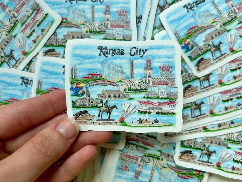Puede incluir: Una pila de pegatinas coloridas con tem&aacute;tica de Kansas City. Cada pegatina presenta un hito o icono diferente de la ciudad, incluyendo el Country Club Plaza, el Nelson-Atkins Museum of Art y el Kauffman Center for the Performing Arts. Las pegatinas est&aacute;n impresas en papel blanco y tienen un acabado brillante.