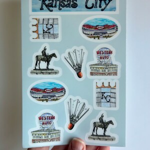 Pode incluir: Um conjunto de nove adesivos com v&aacute;rios marcos e s&iacute;mbolos de Kansas City, Missouri. Os adesivos s&atilde;o impressos em papel branco com fundo azul claro. Os adesivos incluem um est&aacute;dio, uma est&aacute;tua de um cavaleiro a cavalo, um volante e uma placa para Western Auto.