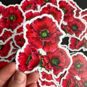 May include: A sheet of red poppy flower stickers. The stickers are printed with a white outline and feature a cluster of three red poppies with green centers.