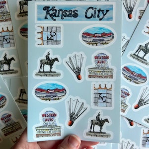 Pode incluir: Uma folha de adesivos com v&aacute;rias imagens relacionadas a Kansas City, incluindo o horizonte da cidade, um est&aacute;dio, uma est&aacute;tua de um cavaleiro a cavalo e um volante. O texto "Kansas City" est&aacute; impresso na parte superior da folha.