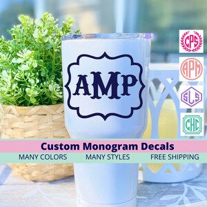 May include: A white tumbler with a navy blue monogram decal featuring the letters "AMP" in a decorative frame. The image also shows examples of other monogram styles and the text "Custom Monogram Decals".