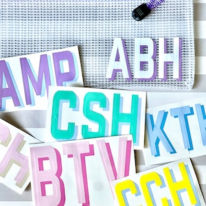 May include: A set of colorful, layered, vinyl letters in various colors, including purple, pink, blue, green, and yellow. The letters spell out the words "AMP", "ABH", "CSH", "KTH", "BTV", and "CCH".
