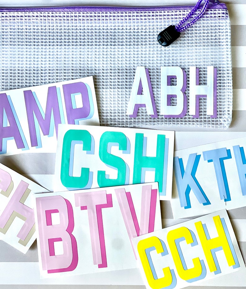 May include: A set of colorful, layered, vinyl letters in various colors, including purple, pink, blue, green, and yellow. The letters spell out the words "AMP", "ABH", "CSH", "KTH", "BTV", and "CCH".