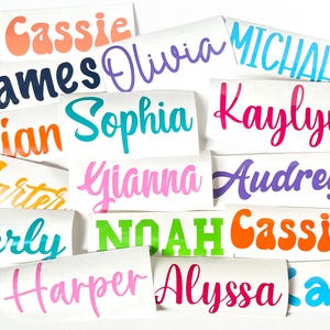 May include: A collection of colorful vinyl stickers with various names written in different fonts and colors. The names include Cassie, James, Olivia, Michael, Lian, Sophia, Kaylyn, Carter, Gianna, Audrey, Ferly, Noah, Cassie, Harper, Alyssa, and Kai.