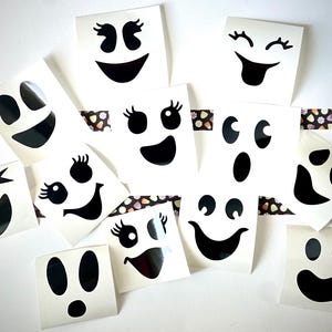 May include: Ten white ghost stickers with different black facial expressions. The stickers are on a white background with a black and white patterned tape.