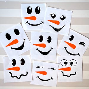 May include: A collection of white square stickers featuring snowman faces. Each sticker has black eyes, an orange carrot nose, and a black smiling mouth. Some stickers have eyelashes or winking eyes. The stickers are arranged on a striped background.