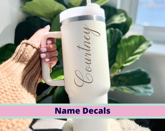 May include: White stainless steel travel mug with a handle and a straw. The mug has the name "Courtney" written on it in gold lettering. Name Decals.