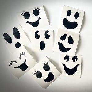 May include: Eight black and white ghost face stickers with different expressions. The stickers are on a white background.