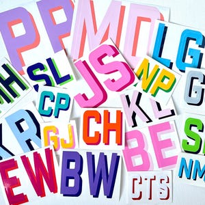 May include: A collection of colorful, outlined letters on white paper. The letters are in various colors, including pink, blue, green, yellow, and orange. The letters are arranged in a random order.