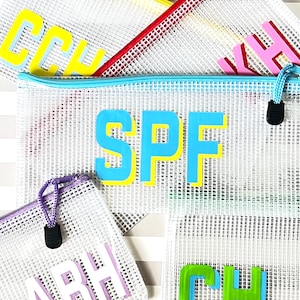 May include: Five mesh zippered pouches with different colored trim and letters. The pouches are white with a grid pattern and have the letters "SPF", "ABH", "CH", "KH", and "CCH" in different colors.