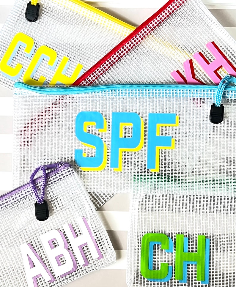 May include: Five mesh zippered pouches with different colored trim and letters. The pouches are white with a grid pattern and have the letters "SPF", "ABH", "CH", "KH", and "CCH" in different colors.