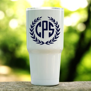 K&ouml;nnte beinhalten: Ein wei&szlig;er Edelstahlbecher mit einem dunkelblauen Monogramm "CPS" in einem Kranz aus Bl&auml;ttern.