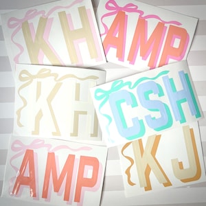 May include: A set of six colorful letters with a bow on each letter. The letters are K, H, A, M, P, and C. The letters are in different colors, including pink, blue, green, and yellow. The letters are on a white background with gray stripes.
