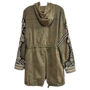 Puede incluir: Una chaqueta verde con capucha y detalles bordados en las mangas. La chaqueta tiene una cintura con cord&oacute;n y una cremallera.