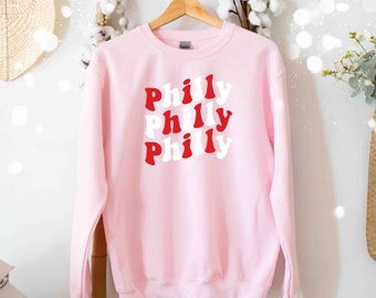 May include: Pink sweatshirt with the word "Philly" repeated three times in a retro font, with red and white letters.
