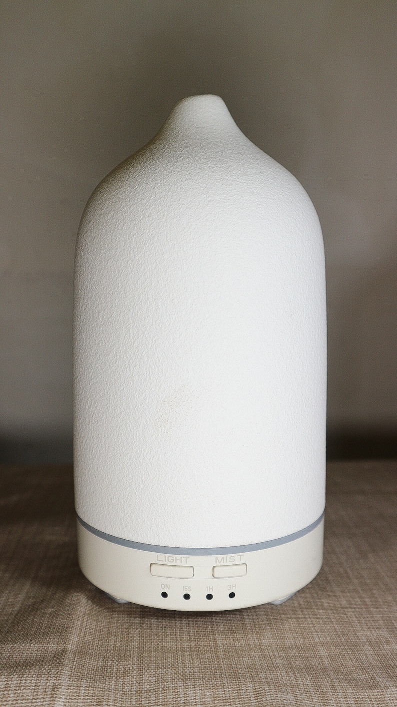 May include: White ceramic essential oil diffuser with a textured surface. It has buttons for light, mist, and timer settings: ON, 15S, 1H, 3H.